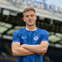 Młody piłkarz Chelsea w niebieskiej koszulce z herbem klubu, z rękami skrzyżowanymi na piersi.