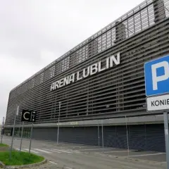Nowoczesny stadion Arena Lublin z napisem na fasadzie. Obok znak parkingu i drogowskazy.