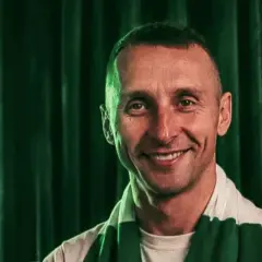 Uśmiechnięty mężczyzna w szaliku Lechii Gdańsk na tle zielonej kurtyny.