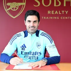 Mikel Arteta, trener Arsenalu, podpisuje dokumenty. Uśmiecha się do aparatu, ubrany w klubowy dres.