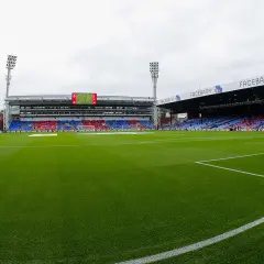Zielona murawa stadionu Selhurst Park, trybuny w kolorach czerwonym i niebieskim, światła masztów.