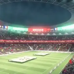 Widok na pełne trybuny stadionu, gdzie kibice wznoszą flagi. Na telebimach widać wynik 00. To z pewnością najładniejszy stadion na świecie.