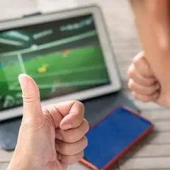 Kciuk w górę i zaciśnięta pięść obok tabletu z meczem piłki nożnej. Tak właśnie można obstawić mecze.
