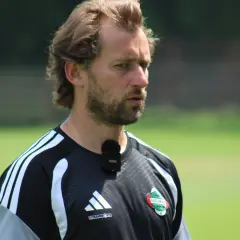 Trener Radomiaka, z mikrofonem na koszulce, skupiony na boisku.