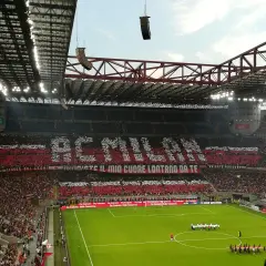 Wielki doping na mediolan stadionie. Trybuny tworzą napis "AC MILAN" i hasło kibiców.