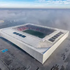 Nowy stadion Odra Opole wyłania się z mgły. Nowoczesna bryła z panelami słonecznymi i czerwonymi trybunami.