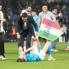 Piłkarz SSC Napoli leży na murawie, otoczony przez kolegów z drużyny i sztab. Włoski klub piłkarski świętuje zwycięstwo.