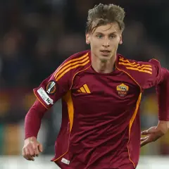 Piłkarz AS Roma w bordowej koszulce z żółtymi pasami, gotowy do gry przeciwko Genoa CFC.