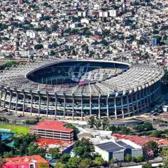 Widok z lotu ptaka na monumentalny stadion Azteca otoczony gęstą zabudową miejską.