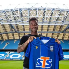 Uśmiechnięty piłkarz Lecha Poznań prezentuje niebieską koszulkę z herbem klubu i logo sponsora STS.