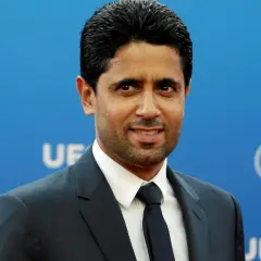 Nasser Al-Khelaifi, właściciel PSG, w garniturze na tle niebieskiej ściany z logo UEFA.