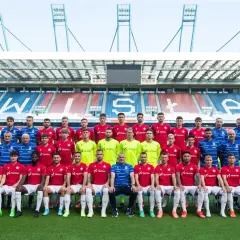Piłkarze Wisły Kraków pozują do wspólnego zdjęcia na tle stadionu.
