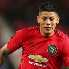 Marcos Rojo w czerwonej koszulce Manchester United, z widocznym logo klubu i sponsora. Jego wiek nie jest widoczny, ale determinacja na twarzy mówi wszystko.