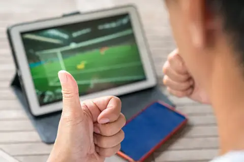Kciuk w górę i zaciśnięta pięść obok tabletu z meczem piłki nożnej. Tak właśnie można obstawić mecze.