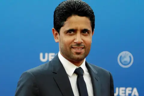 Nasser Al-Khelaifi, właściciel PSG, w garniturze na tle niebieskiej ściany z logo UEFA.