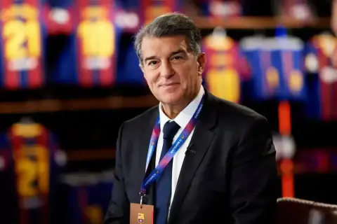 Prezes FC Barcelona, Joan Laporta, w garniturze, z identyfikatorem klubu na szyi. W tle widoczne koszulki piłkarskie.