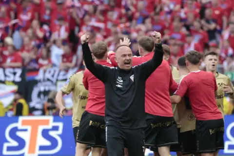 Trener Górnika Zabrze świętuje z drużyną. W tle kibice w barwach Górnika.