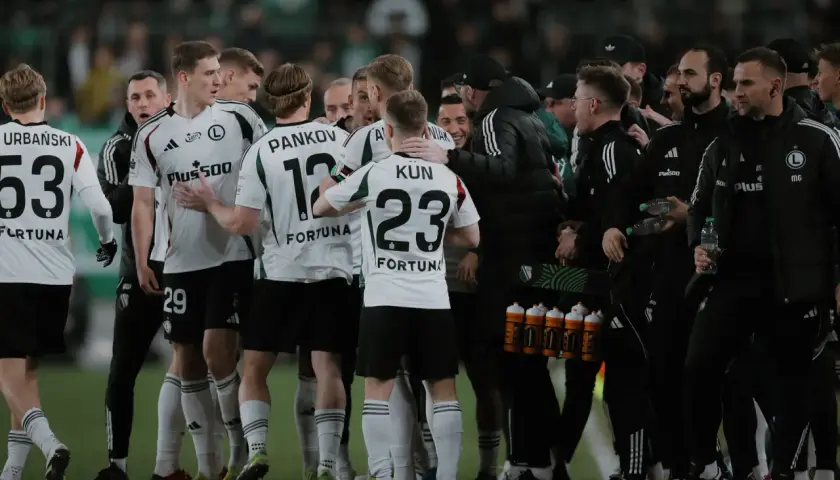 Legia Warszawa zawodnicy w białych strojach świętują na boisku. Widać numery 53, 29, 12 i 23.