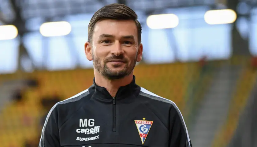 Uśmiechnięty trener Górnika Zabrze w czarnej bluzie z logo klubu.