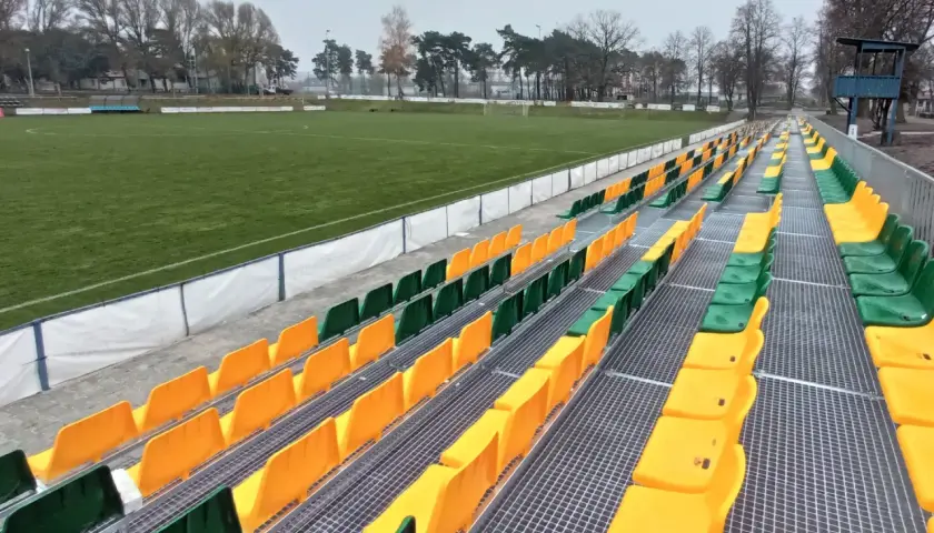 Puste trybuny stadionu Lechii Zielona Góra, z rzędami zielonych i żółtych krzesełek, czekają na kibiców.