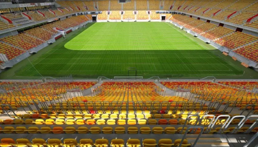 Pusta trybuna stadionu Jagiellonii, z żółtymi i czerwonymi siedzeniami, czeka na kibiców. Pojemność stadionu robi wrażenie.