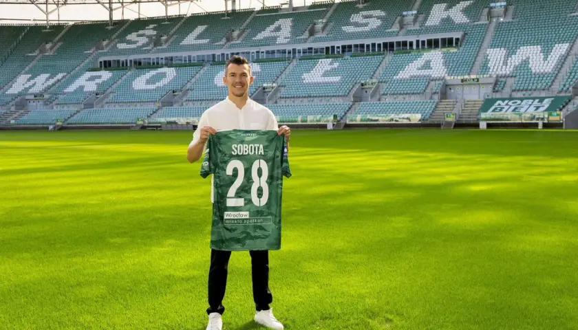 Piłkarz z koszulką "Sobota 28" na tle stadionu. To jeden z nowych śląsk wrocław transfery.