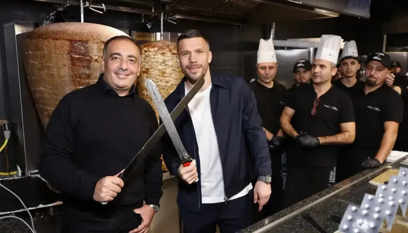 Lukas Podolski z nożami w ręku, obok niego pracownicy restauracji z kebabem.