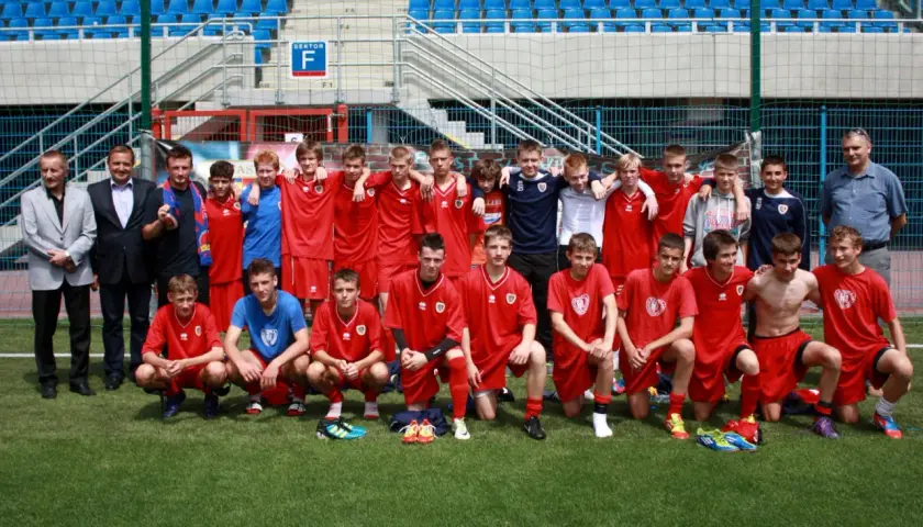 Piast Gliwice zawodnicy w czerwonych strojach pozują do zdjęcia na boisku.