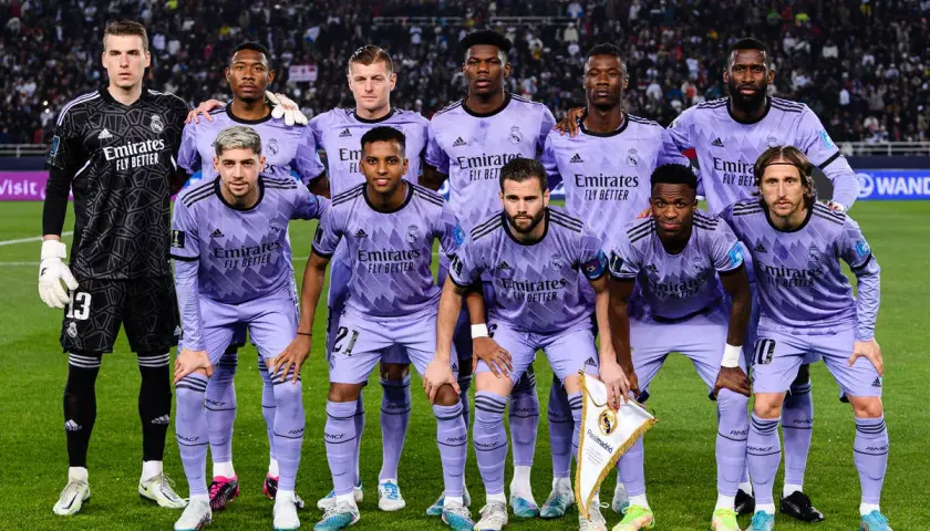 Drużyna pilkarze Real Madryt w fioletowych strojach pozuje do zdjęcia na murawie stadionu.