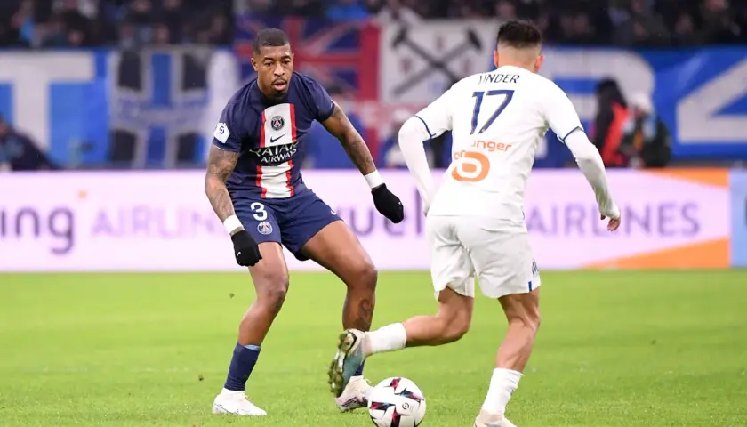 Kimpembe w ciemnym stroju PSG walczy o piłkę z zawodnikiem w białej koszulce.