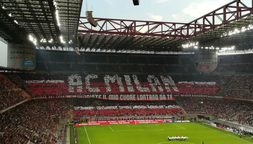 Wielki doping na mediolan stadionie. Trybuny tworzą napis "AC MILAN" i hasło kibiców.