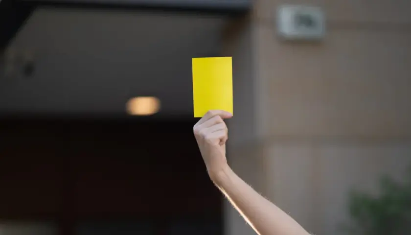 Ręka trzymająca żółtą kartkę, jak w piłce nożnej.
