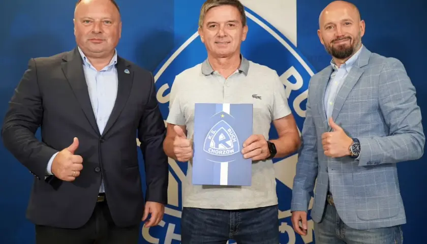 Trzech mężczyzn pozuje do zdjęcia z dokumentem K.S. Ruch Chorzów. Jeden z nich, nowy trener ruchu chorzów, trzyma dokument.