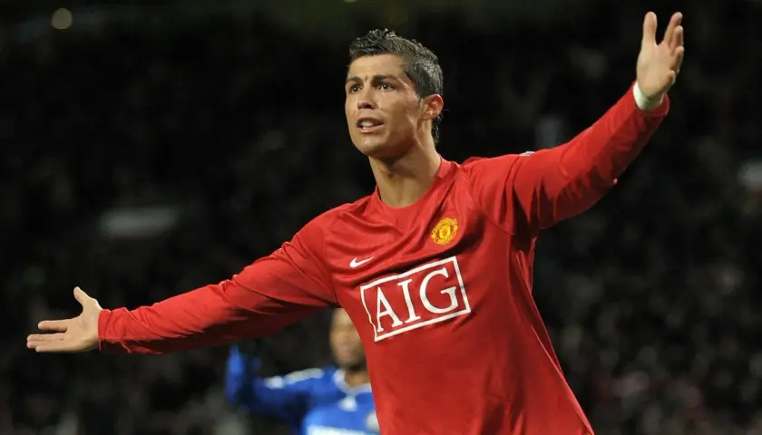 Cristiano Ronaldo w czerwonej koszulce Manchesteru United, z uniesionymi rękami, świętuje bramkę. To był kluczowy moment przed jego transferem.