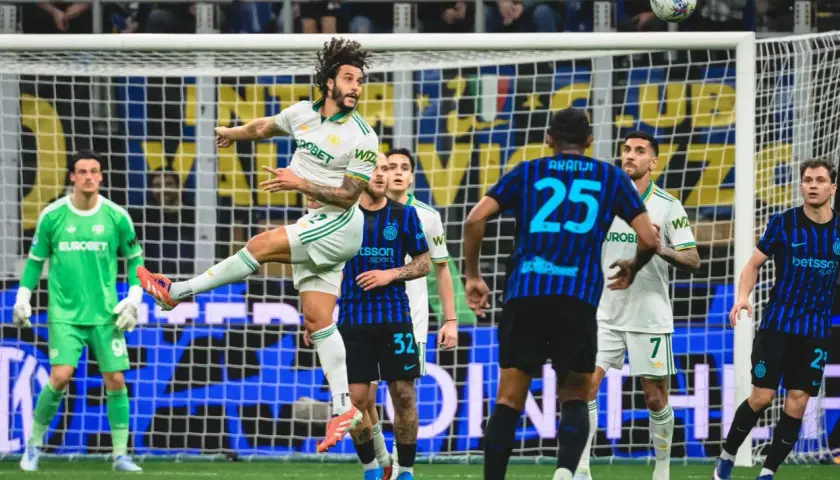 Piłkarz w białej koszulce wyskakuje do główki podczas meczu Inter Mediolan – AS Roma. Bramkarz w zielonym stroju czeka na rozwój akcji.