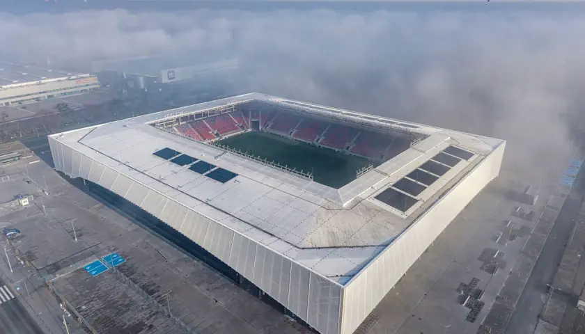 Nowy stadion Odra Opole wyłania się z mgły. Nowoczesna bryła z panelami słonecznymi i czerwonymi trybunami.