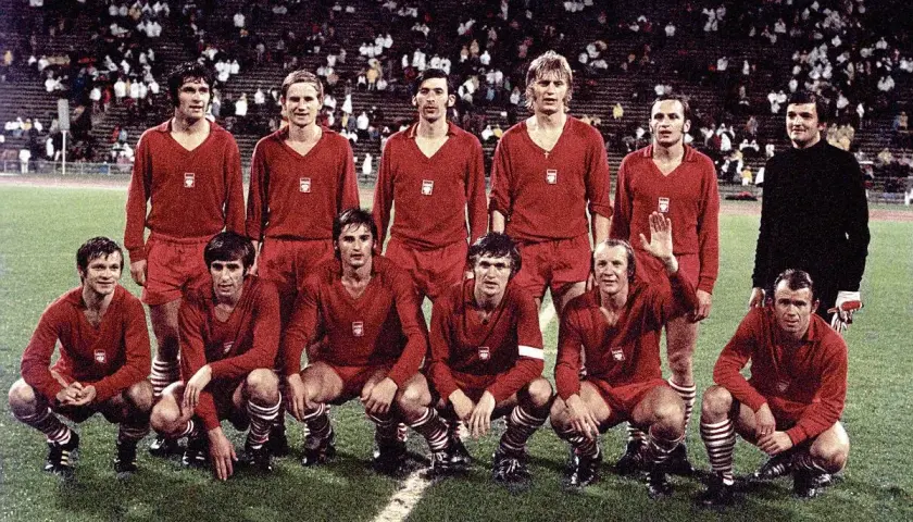 Byli piłkarze reprezentacji Polski w czerwonych strojach pozują na boisku.