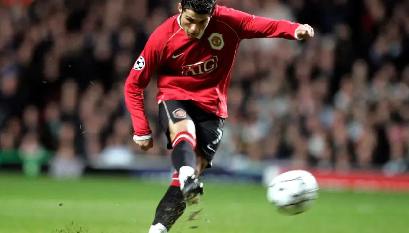 Cristiano Ronaldo w czerwonej koszulce Manchesteru United, z numerem na koszulce, kopie piłkę.