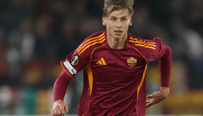 Piłkarz AS Roma w bordowej koszulce z żółtymi pasami, gotowy do gry przeciwko Genoa CFC.