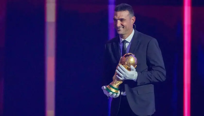 Uśmiechnięty trener Argentyny, Lionel Scaloni, trzyma Puchar Świata w złotych rękawiczkach.