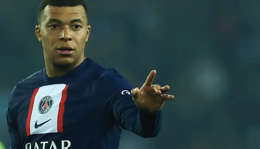 Kylian Mbappé w koszulce PSG, gdzie gra, pokazuje gest dłonią.
