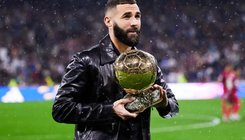 Karim Benzema trzyma Złotą Piłkę, zastanawiając się, ile waży złota piłka.