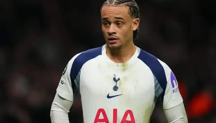Jeden z tottenham zawodnicy w białej koszulce z granatowymi rękawami, z charakterystyczną fryzurą i skupionym wyrazem twarzy.