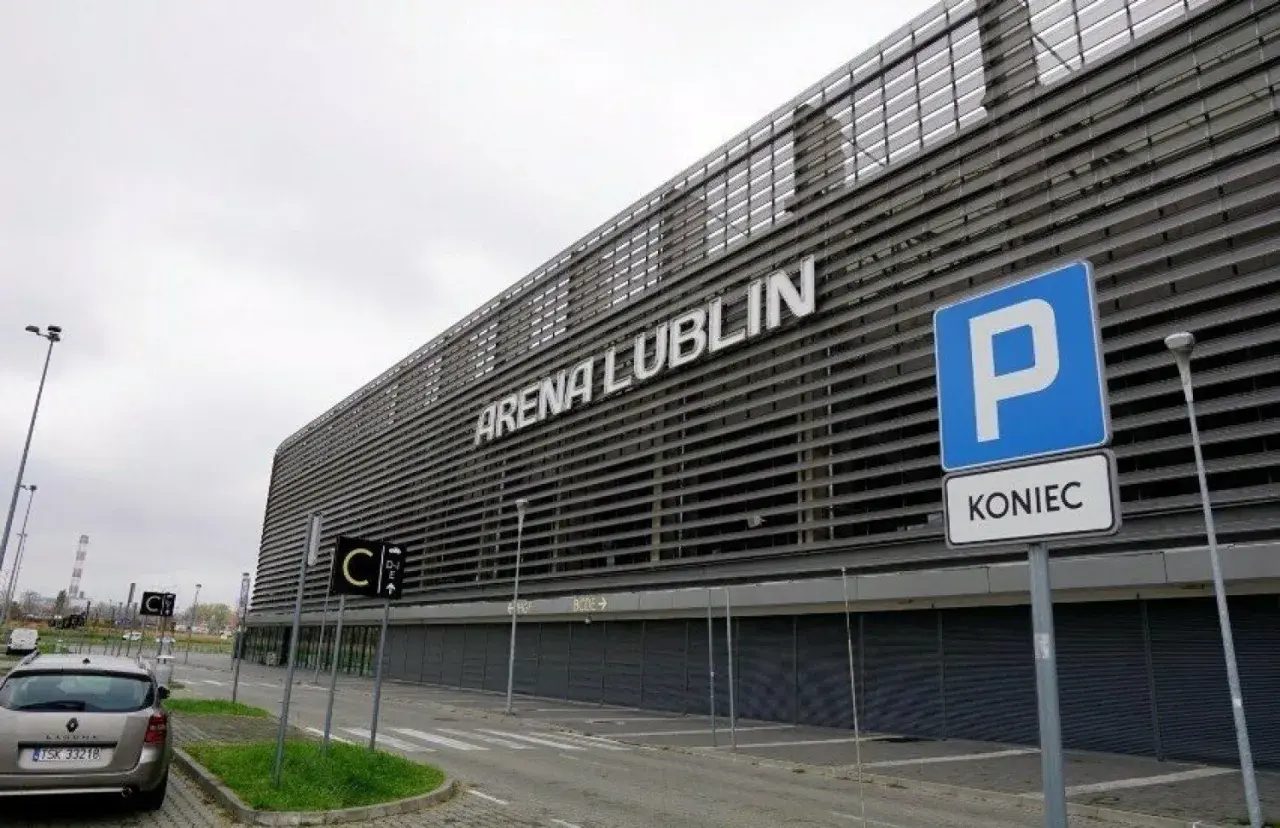 Nowoczesny stadion Arena Lublin z napisem na fasadzie. Obok znak parkingu i drogowskazy.