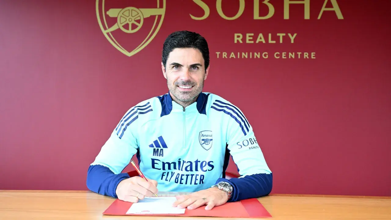 Mikel Arteta, trener Arsenalu, podpisuje dokumenty. Uśmiecha się do aparatu, ubrany w klubowy dres.