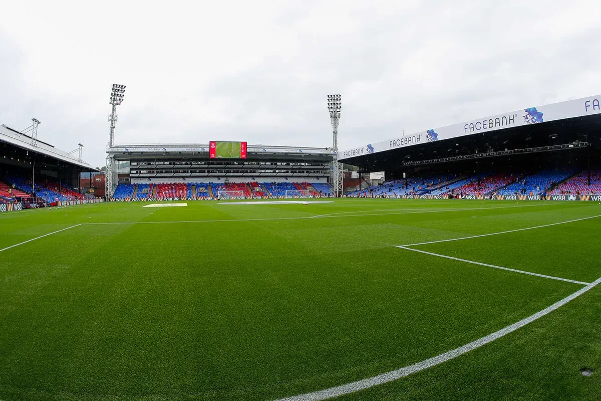 Zielona murawa stadionu Selhurst Park, trybuny w kolorach czerwonym i niebieskim, światła masztów.