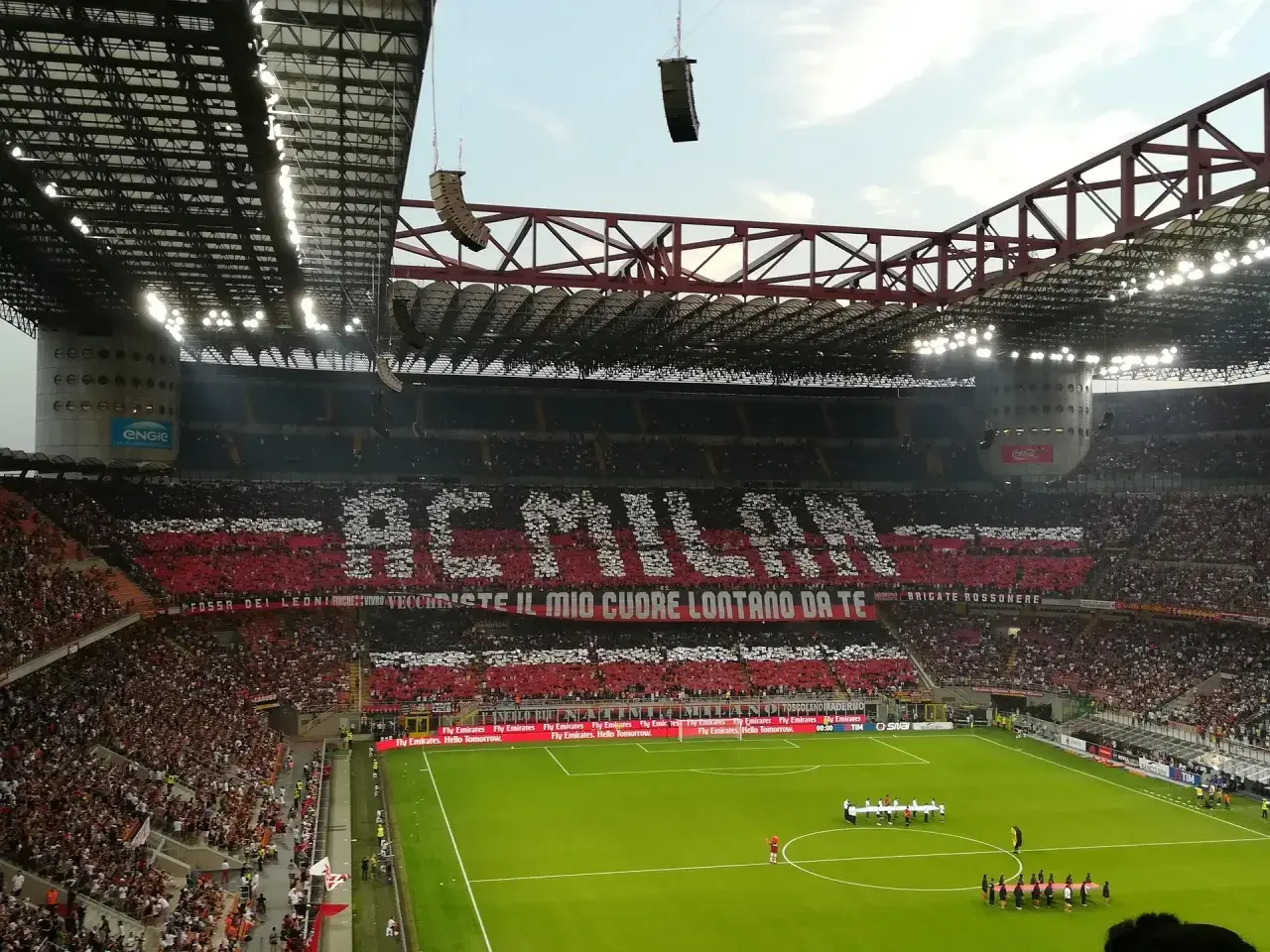 Wielki doping na mediolan stadionie. Trybuny tworzą napis "AC MILAN" i hasło kibiców.