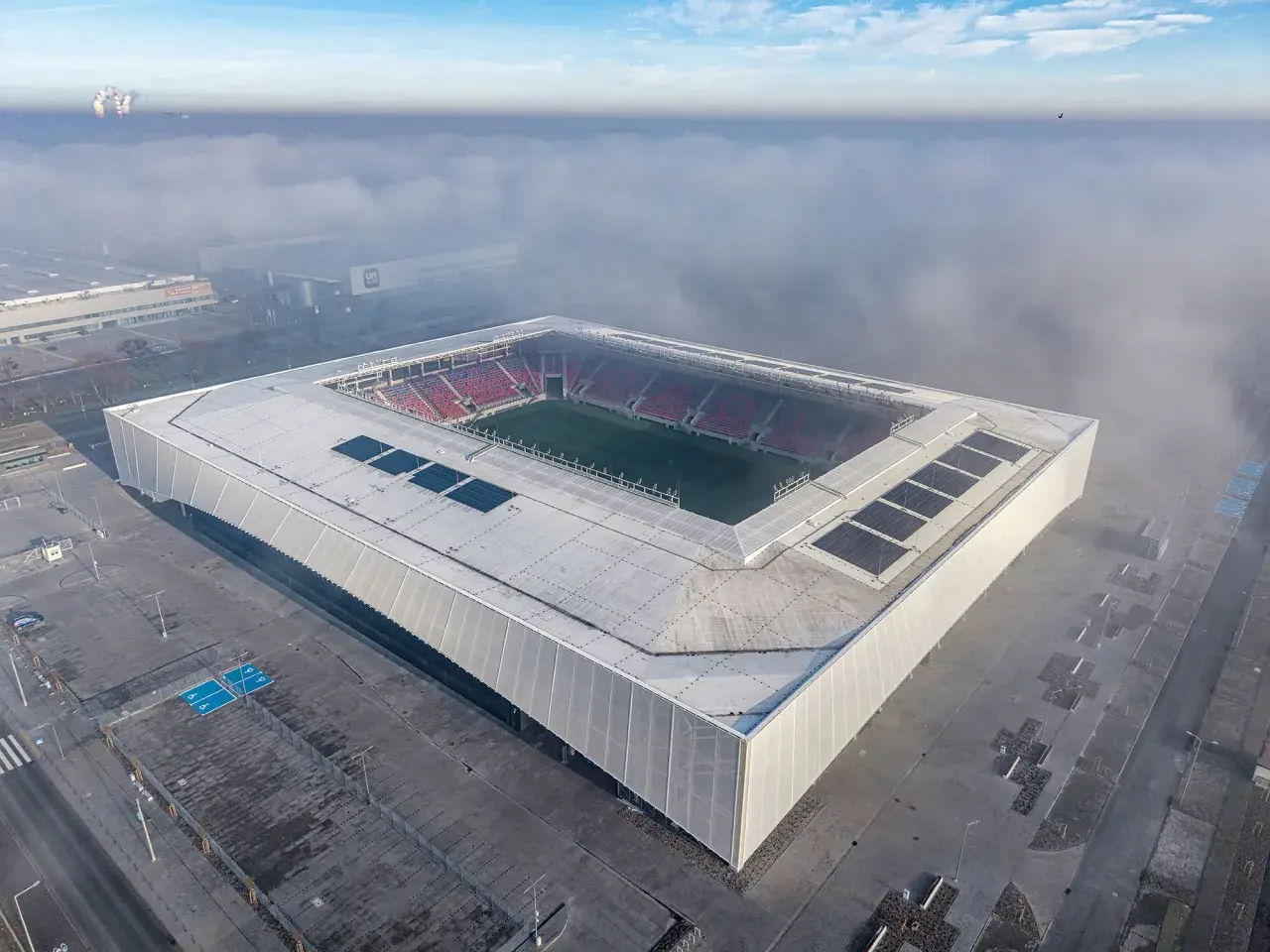 Nowy stadion Odra Opole wyłania się z mgły. Nowoczesna bryła z panelami słonecznymi i czerwonymi trybunami.