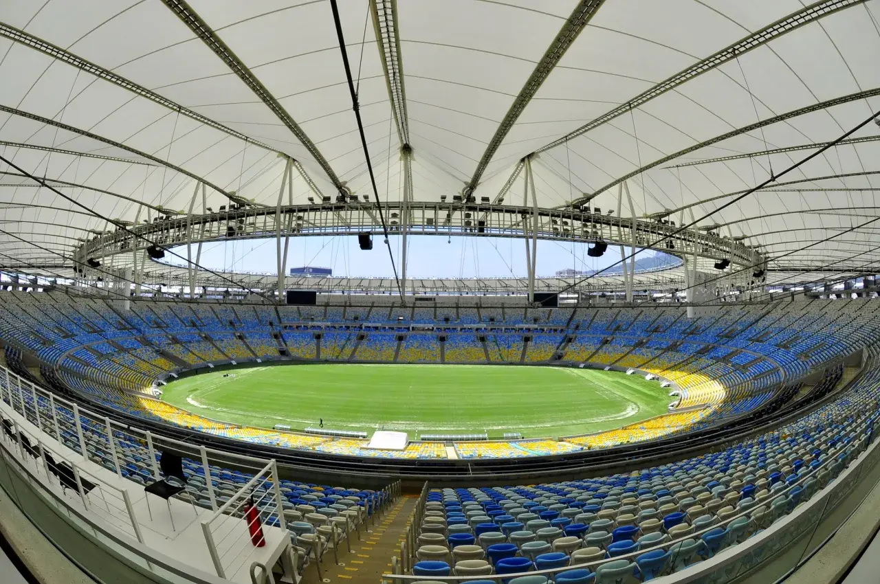 Pusta Marakana, stadion w Rio de Janeiro, z zieloną murawą i niebiesko-żółtymi trybunami pod białym dachem.