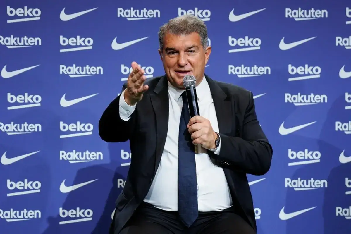 Joan Laporta, właściciel Barcelony, przemawia do mikrofonu na tle niebieskiej ścianki z logo klubu i sponsorów.